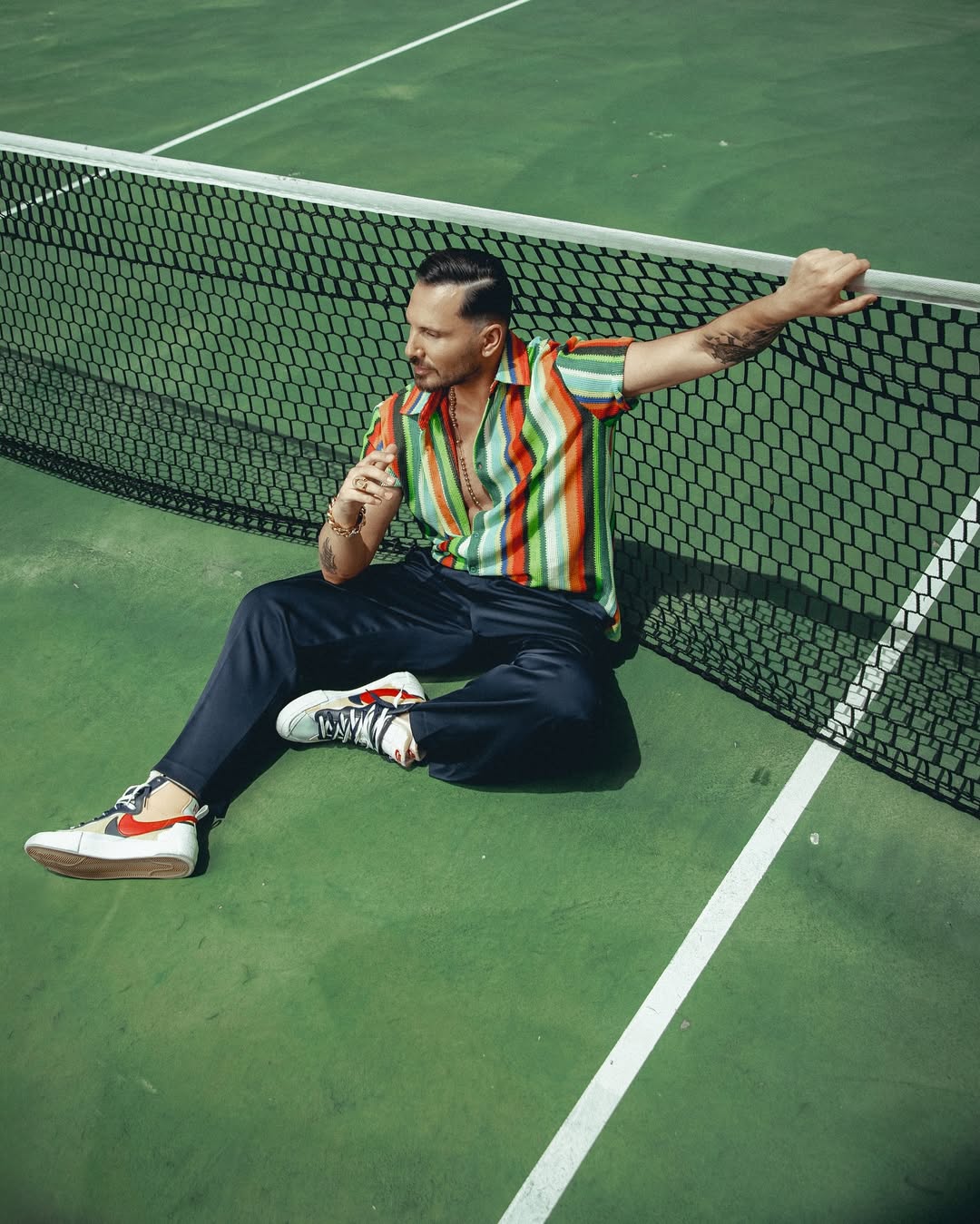 Lebanese actor Carlos Azar in a casual, outdoor portrait, wearing sunglasses and a cream sweater, photographed by Jean-Claude Dib.